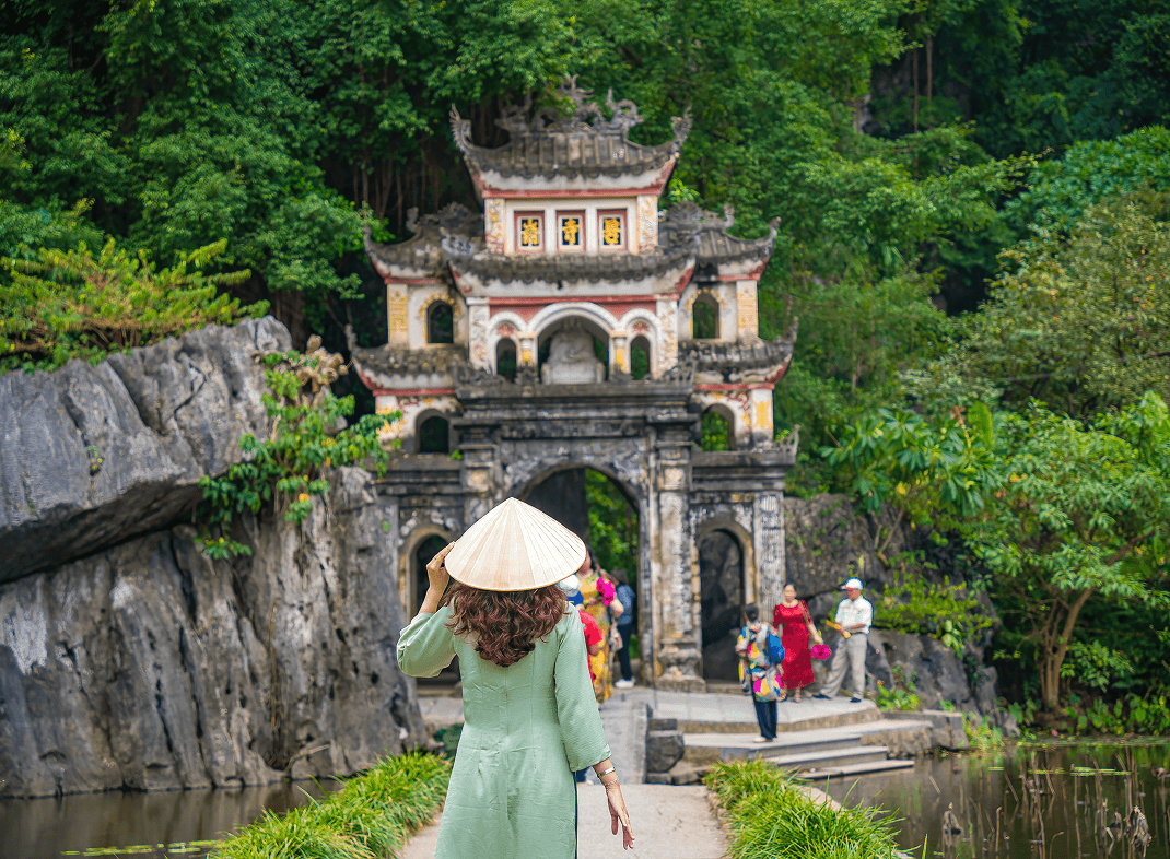 back-view-girl-wearing-ao-dai-front-outdoor-park-landscape-with-lake-stone-bridge-gate-entrance-ancient-bich-dong-pagoda-complex-ninh-binh-vietnam-travel-destination 1